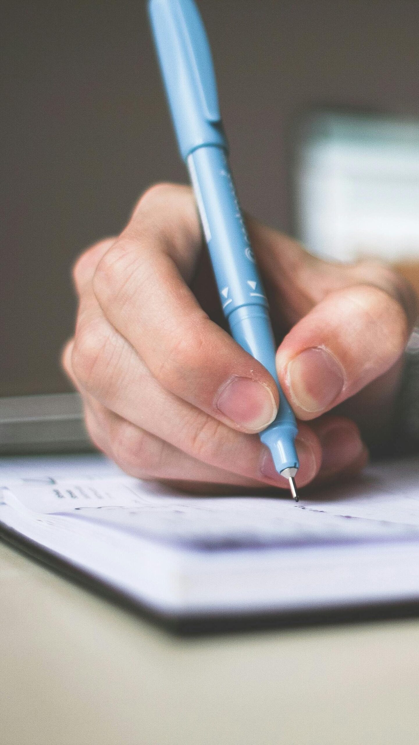 Close-up of hand writing in notebook using a blue pen, focus on creativity.